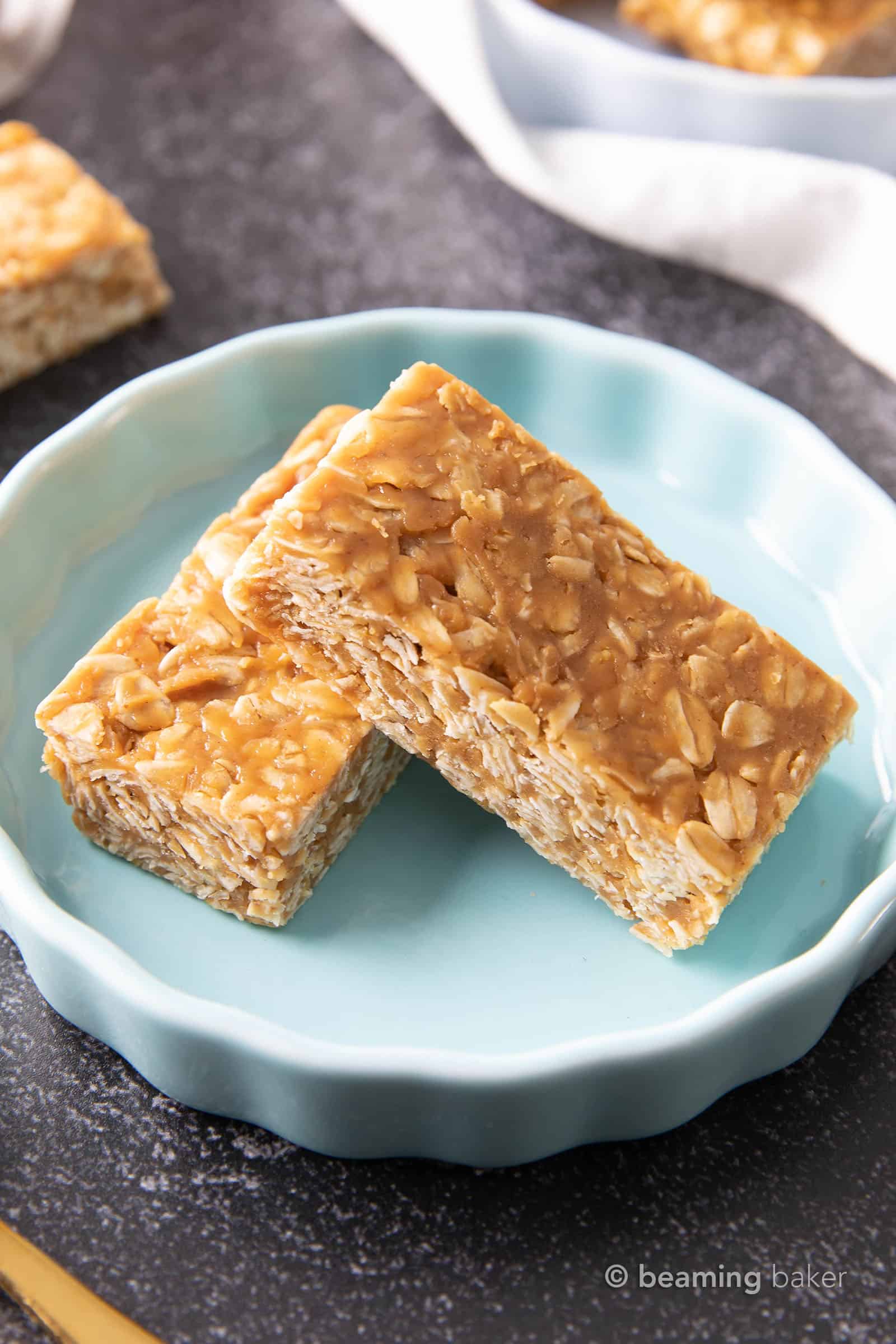 Two granola bars stacked on top of each other in a blue dish, sitting on a dark gray table.
