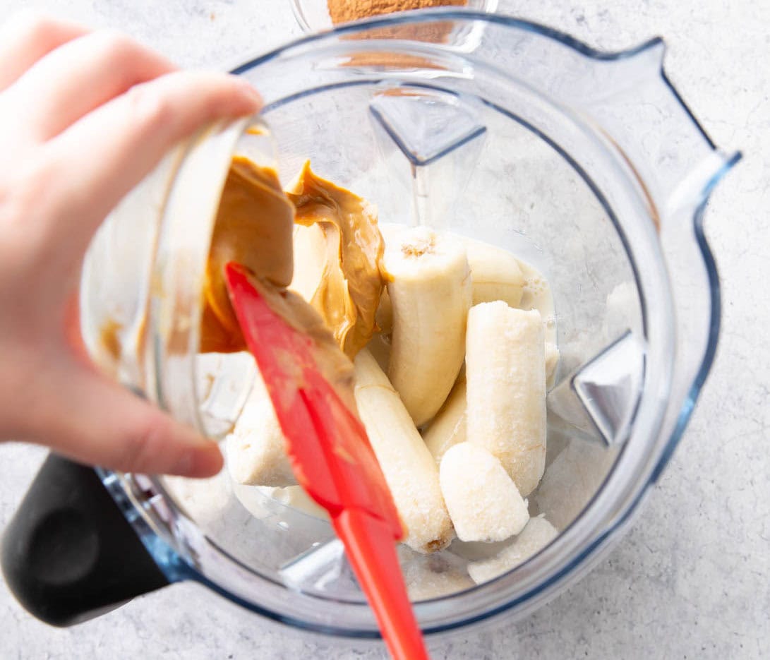 Scraping ingredients out of prep bowls to add to a blender to make this chocolate peanut butter banana smoothie recipe