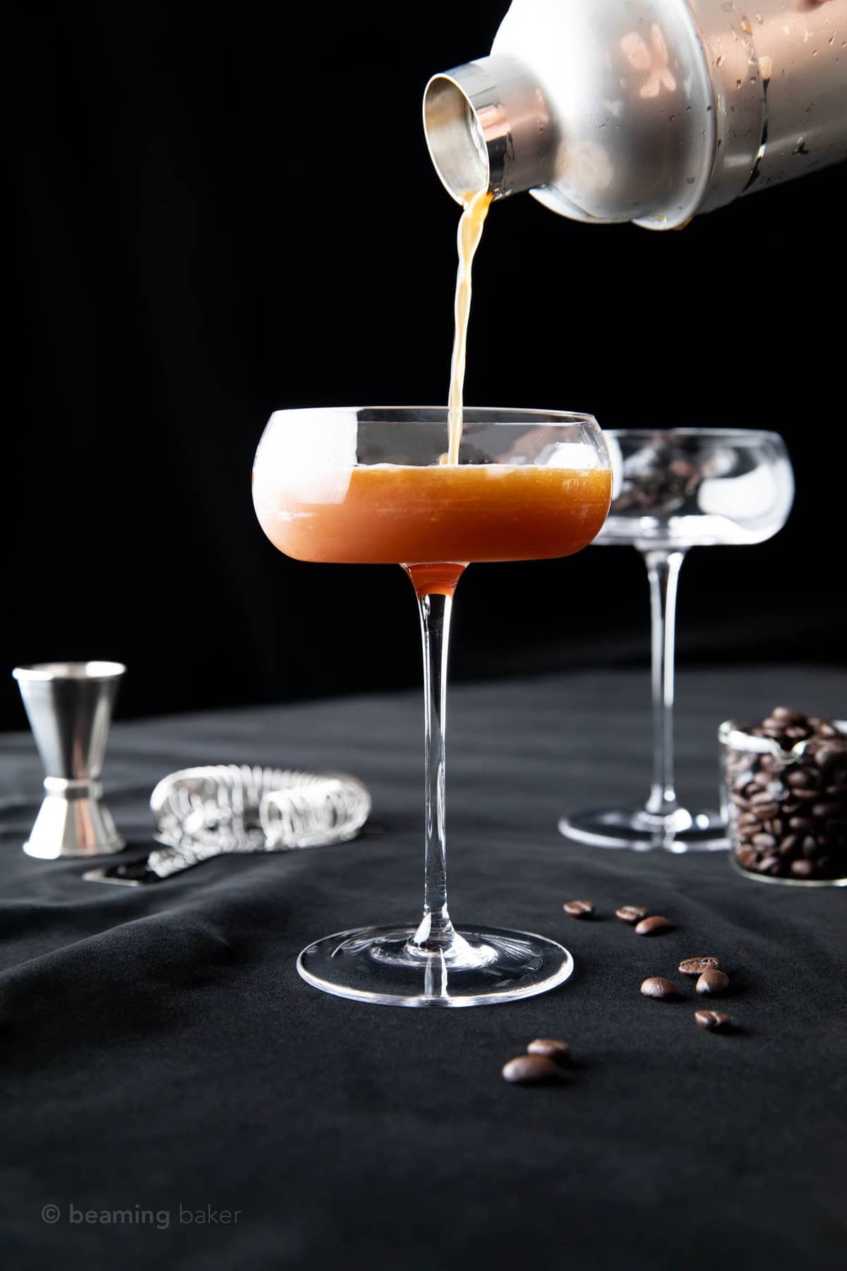 halfway through pouring the cocktail mixture into a coupe glass
