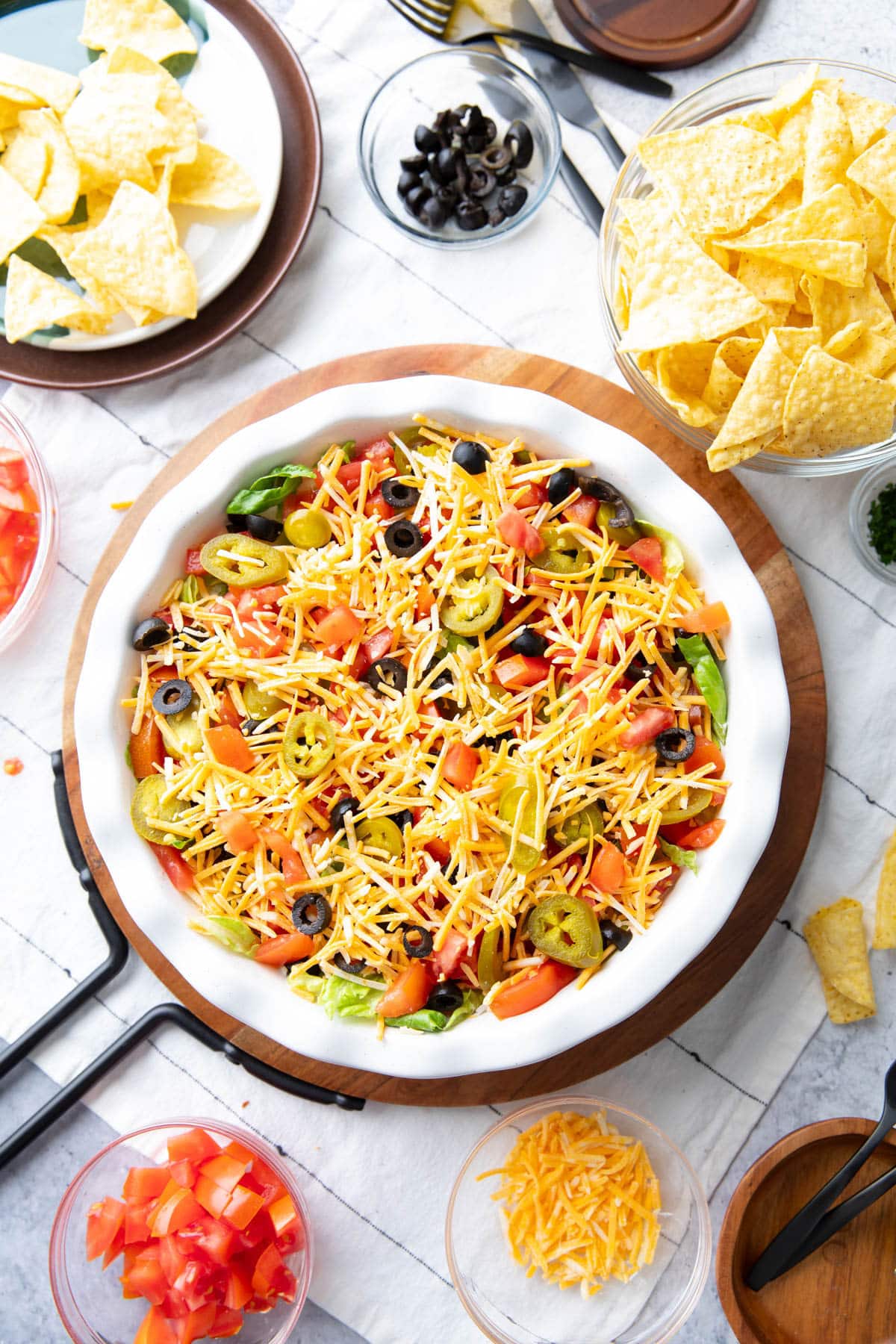 Top view of taco dip in a pie pan topped with shredded cheese, lettuce, tomatoes, jalapeños, and sliced olives.