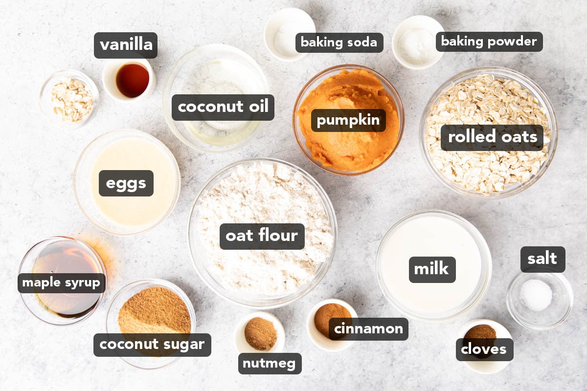 Healthy Pumpkin Oatmeal Muffins ingredients laid out on a table in bowls, including pumpkin puree, flour, coconut oil, rolled oats, and more.