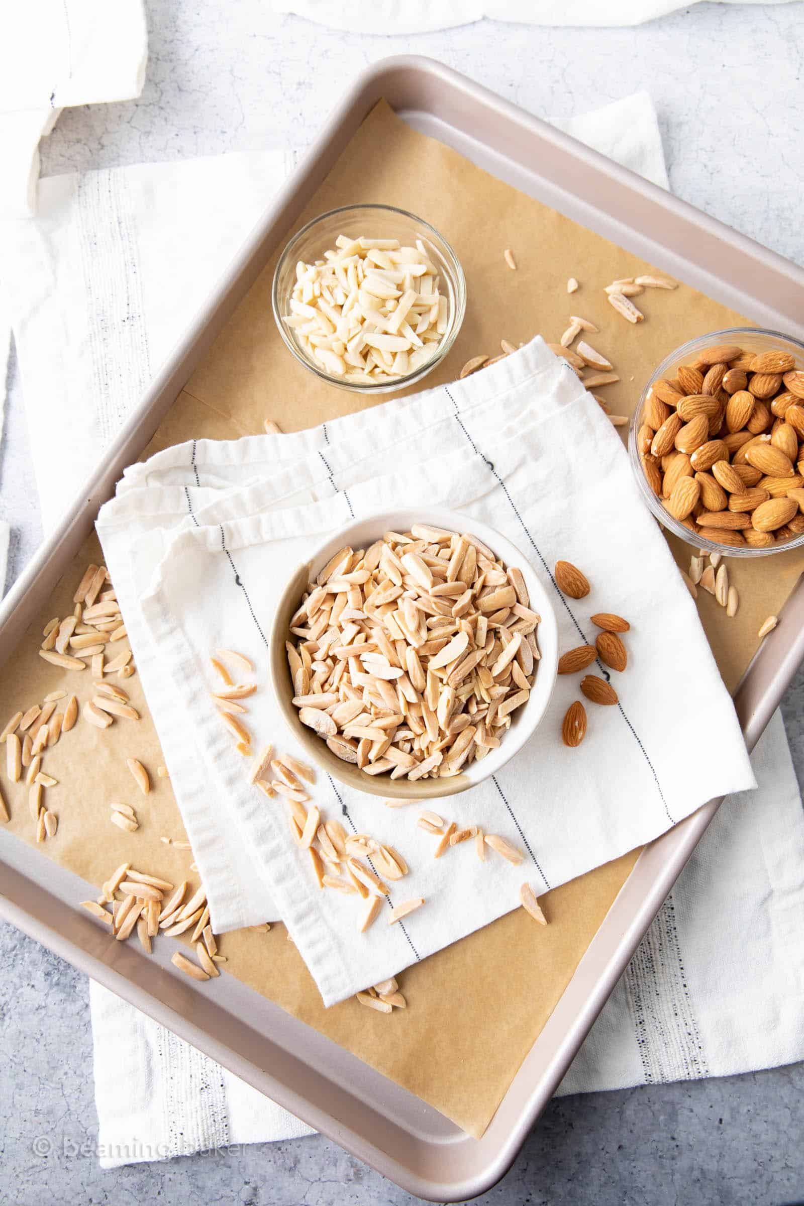 kitchen table with baking supplies for learning how to toast slivered almonds including slivered almonds whole almonds and bowl of toasted slivered almonds
