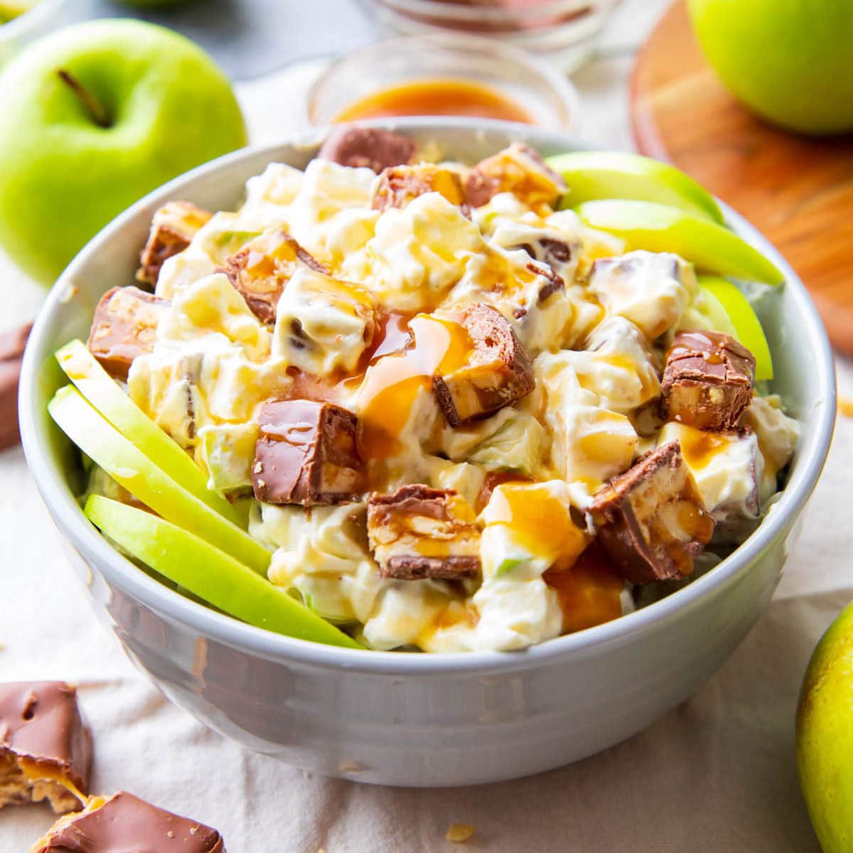 featured image with Snickers Salad served with caramel sauce, apple slices, and Snickers.