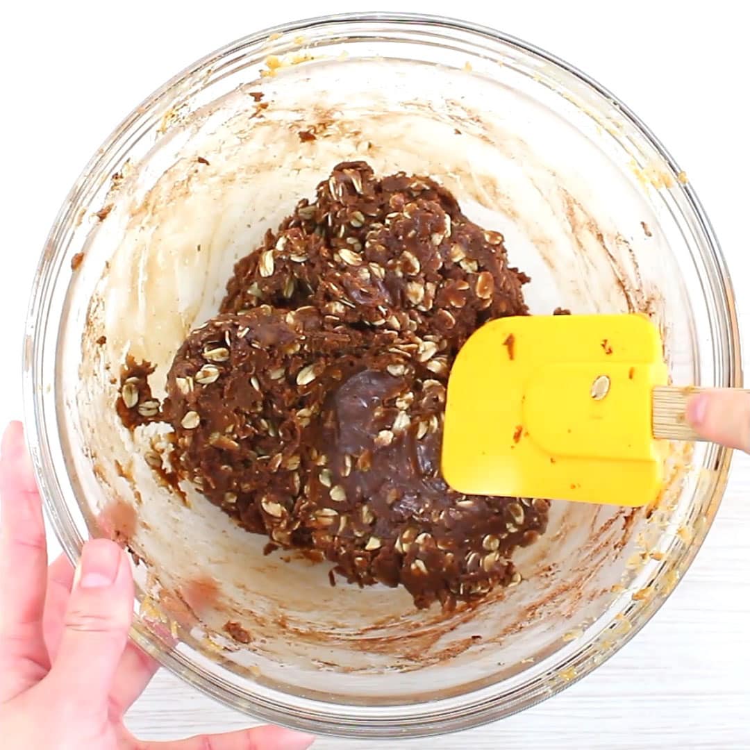 hand holding a spatula to finish folding no bake chocolate oatmeal cookies dough