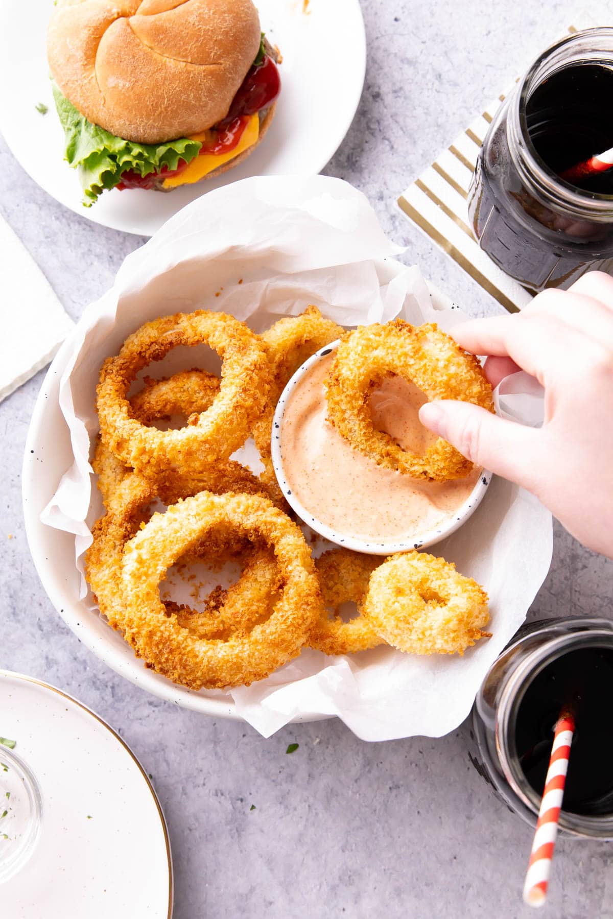 Dipping an appetizer into a bowl of sauce served on a table with a burger and glasses of soda at a diner.