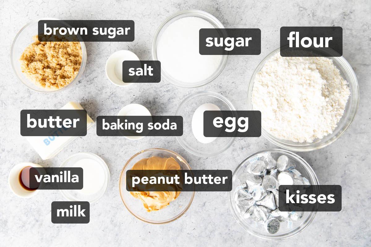 Ingredients for this peanut butter blossoms recipe measured into bowls, including peanut butter, Hershey’s kisses, flour, egg, butter, vanilla, sugar, and more.