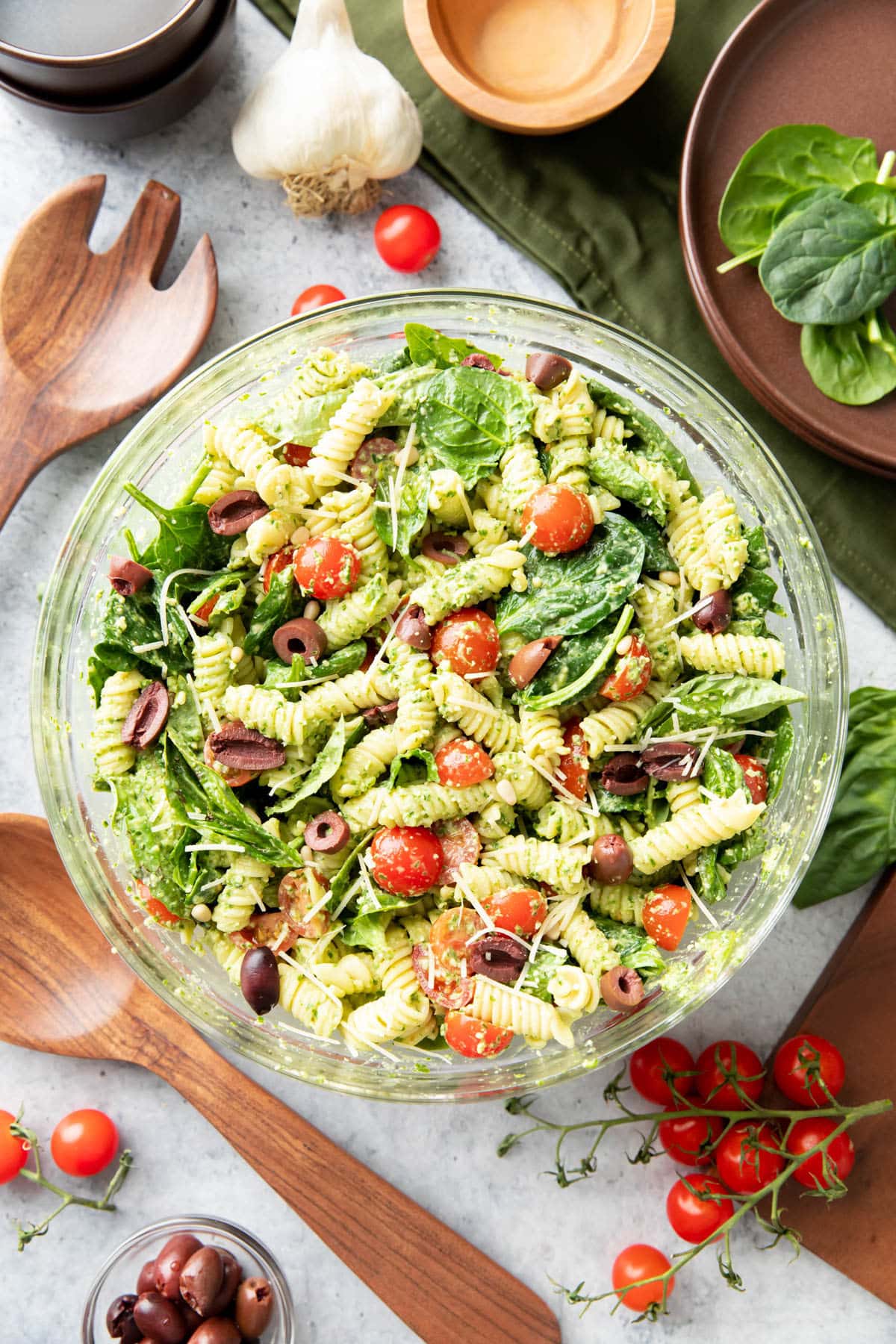 pesto pasta salad in mixing bowl with grated parmesan and kalamata olives