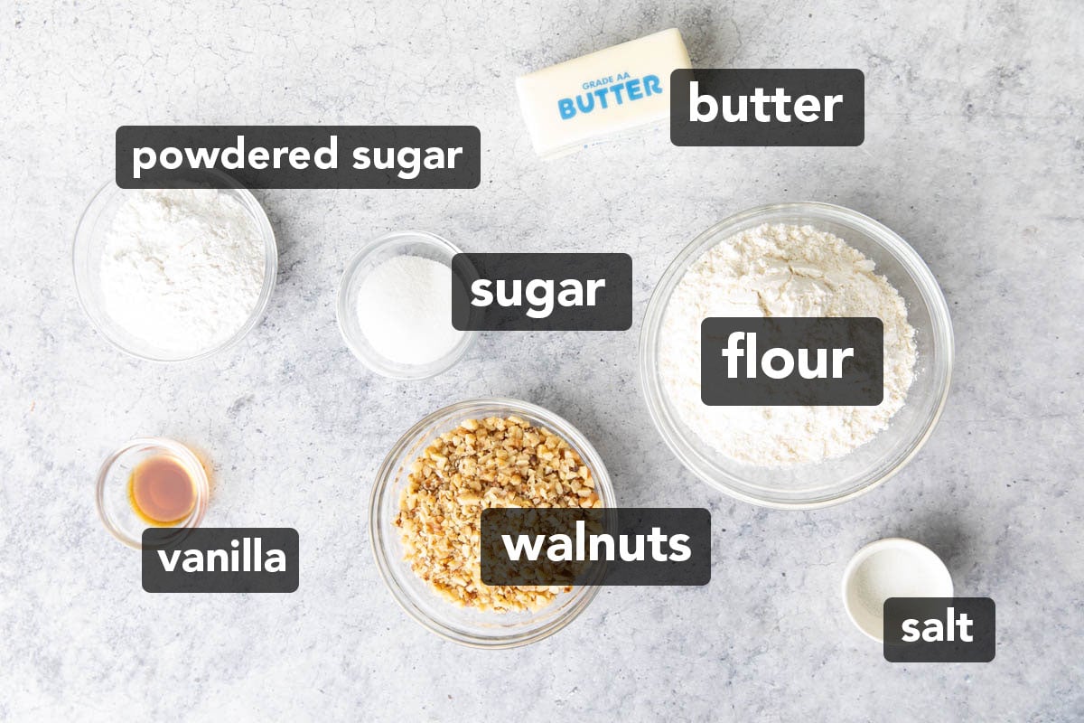 Ingredients in the recipe for snowball cookies with walnuts recipe measured into glass bowls including walnuts, flour, butter, sugar, and powdered sugar